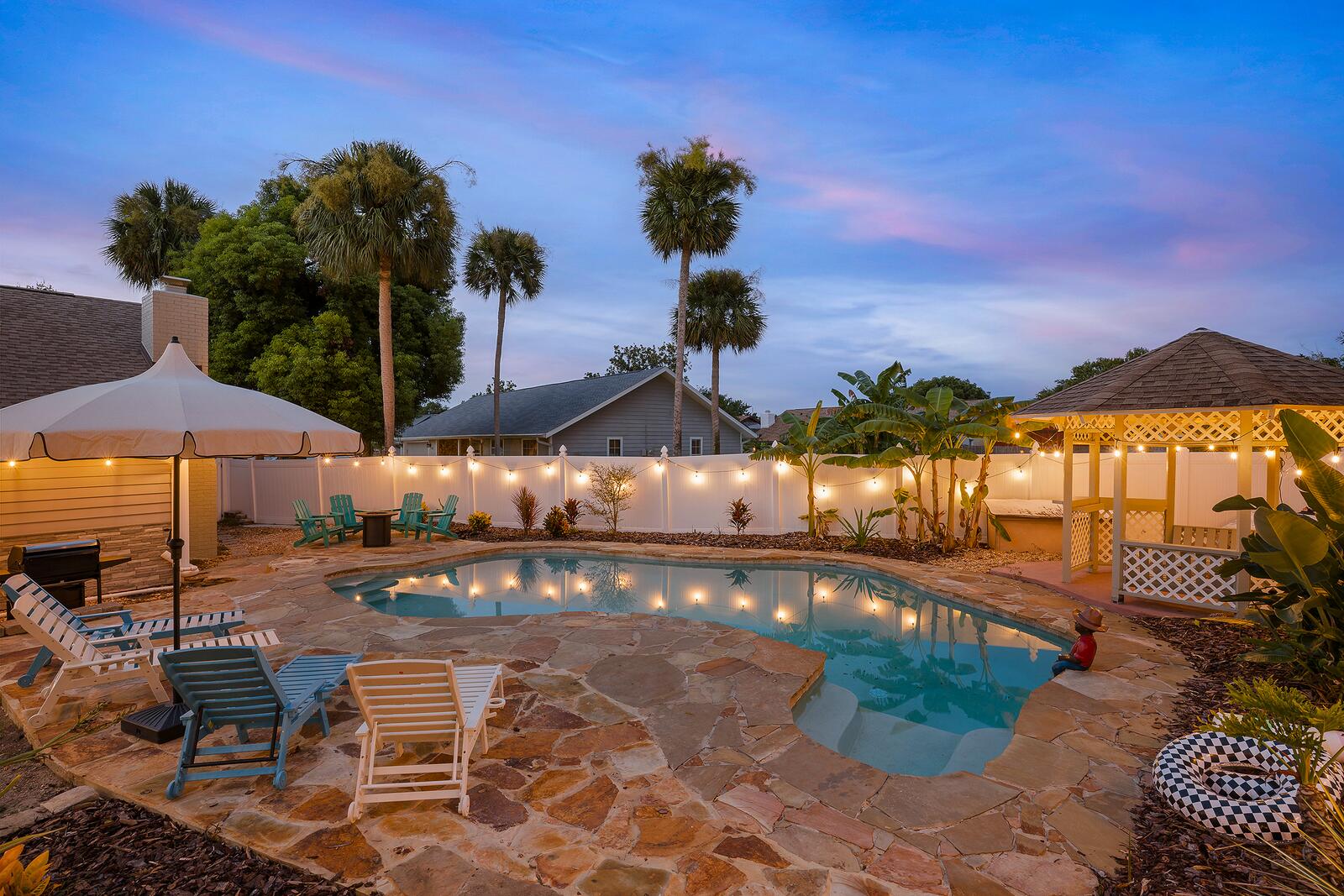 Pool, gazebo, and string lights at dusk in the fenced backyard