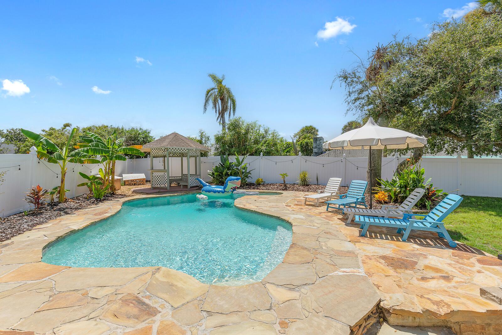 Private free-form pool with string lights and palms in a fenced backyard